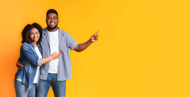 istock Positive Black Spouses Cuddling and Pointing At Copy Space On Yellow Background 1256495250
