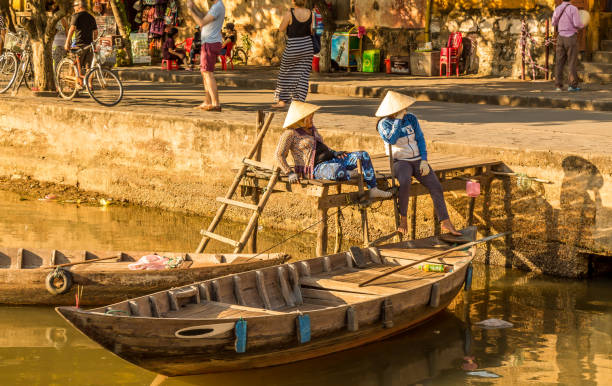 Two vietnamese ladies with conical hats relaxing by the river Two vietnamese ladies with conical hats relaxing by the river and their boats, Hoi An, Vietnam - Hoi An, Vietnam - January 10th, 2015 thu bon river stock pictures, royalty-free photos & images