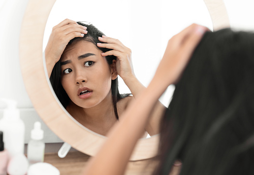 Mujer asiática preocupada revisando su cabello en el espejo en casa photo