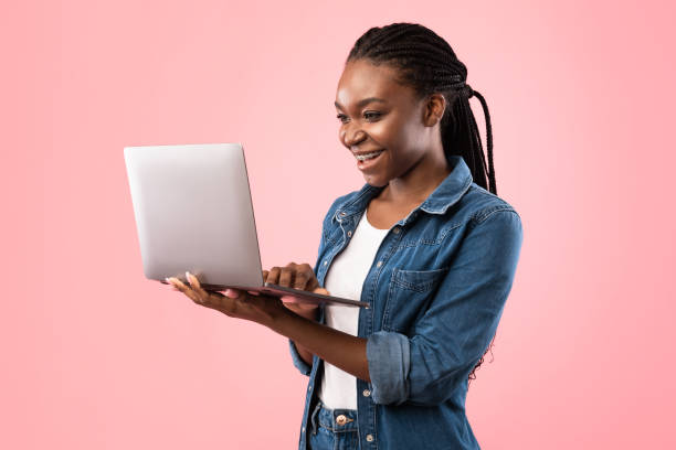 istock Cheerful Black Woman Using Laptop Standing On Pink Background 1256498958