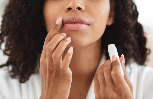 Lip Care. Unrecognizable black woman applying moisturising chapstick on lips, cropped image, closeup