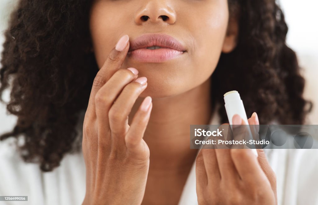 Lip Care. Unrecognizable black woman applying moisturising chapstick on lips, closeup Lip Care. Unrecognizable black woman applying moisturising chapstick on lips, cropped image, closeup Human Lips Stock Photo