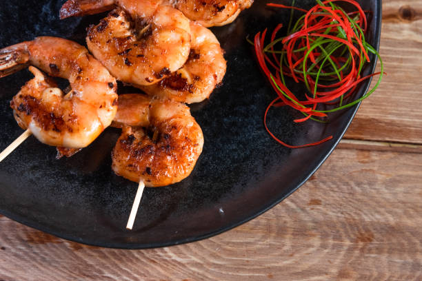 istock Appetizing fried shrimp on a skewer in a black plate on a wooden surface among lemon and seasonings. The concept of fast and wholesome food 1256502368