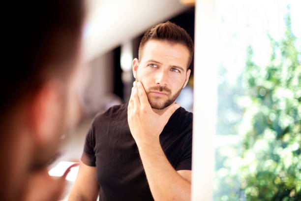 istock Handsome young man standing in front of bathroom mirror and looking his face 1256509595