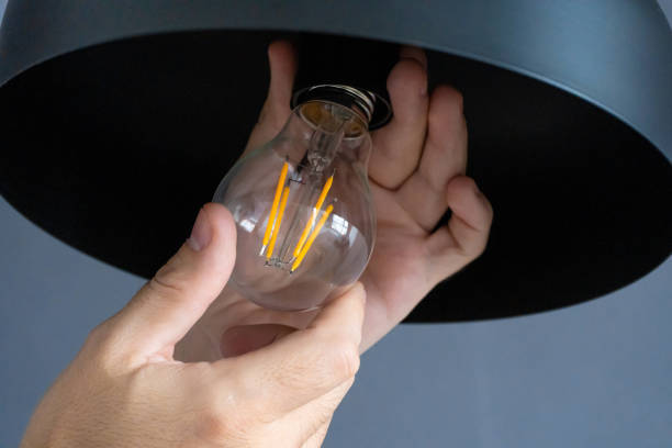 Close-up. A hand changes a light bulb in a stylish loft lamp. Spiral filament lamp. Modern interior decor.