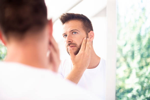 istock Handsome young man standing in front of bathroom mirror and looking his face 1256509680