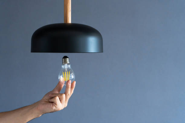 istock Close-up. A hand changes a light bulb in a stylish loft lamp. Spiral filament lamp. Modern interior decor. 1256509735
