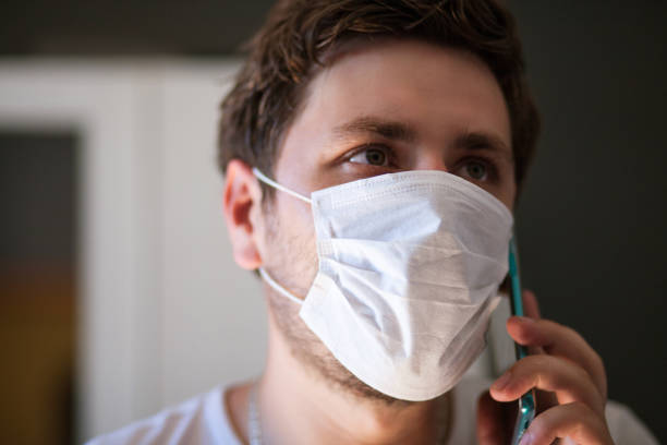 istock Coronavirus. Covid-19. Man in quarantined wearing protective mask using phone 1256511636