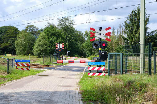 Closed railway crossing with closed barriers and blinking red lights. Blue warning sign with dutch text Wait at red sign. The Netherlands, Bennekom