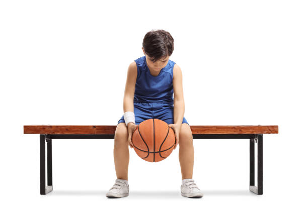 istock Sad little boy sitting on a bench with a basketball 1256516482