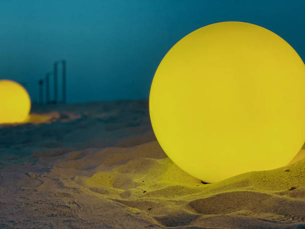 Abstract two artificial moons on the sand, two round lamps with soft light on the evening beach as an element of landscape design.