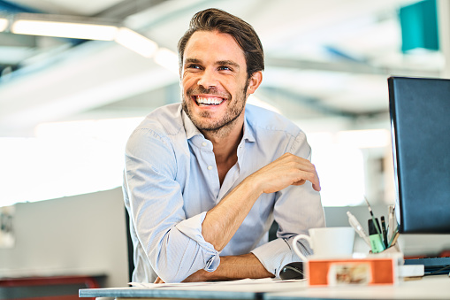 Young businessman laughing while working at his desk in a large modern office space