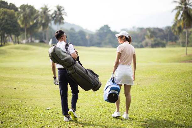 asiatische chinesische paar zu fuß zusammen auf dem golfplatz mit ihren golftaschen. - playing golf fotos stock-fotos und bilder