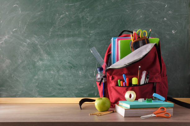 istock Backpack full of school supplies on table and blackboard front 1256524211