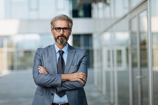 Portrait of a mature bearded businessman with glasses standing in front of an office building