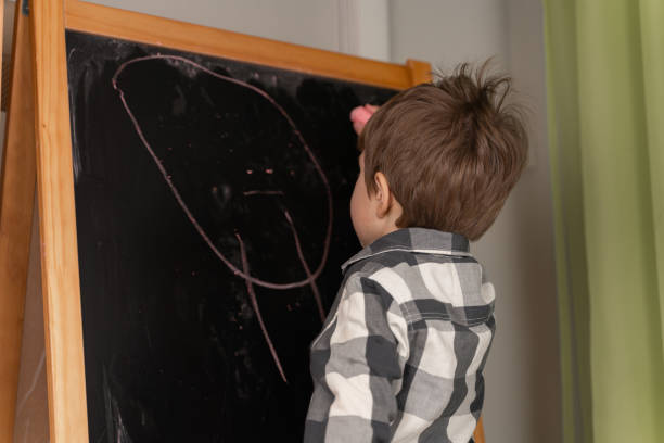 istock Little boy draws chalk on school board 1256527949
