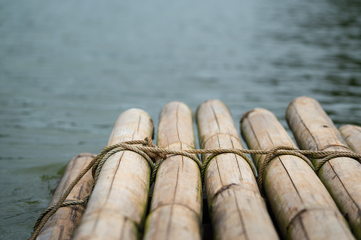 Bamboo rafting stacked which is binding with rope line, it's floating on the lake water. Journey or adventure activity. Transportation object. Selective focus on the rope surface.