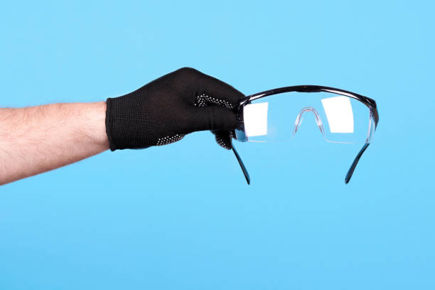 istock Hand with working glove holding protective glasses. Isolated on blue background. 1256532044