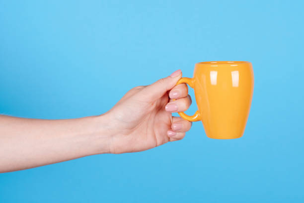 istock Hand with yellow coffee mug. Isolated on blue background. 1256532192