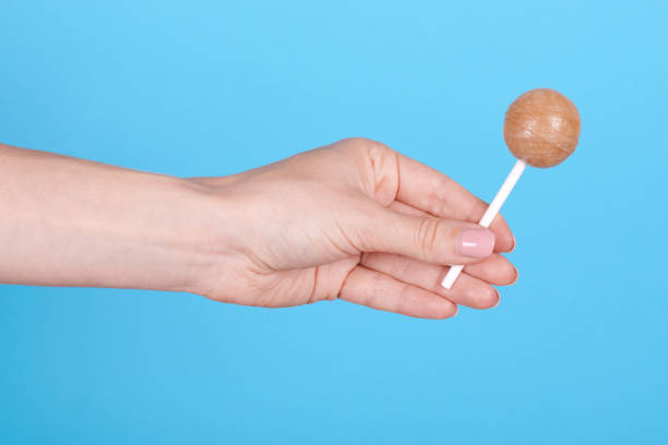istock Hand with sweet caramel lollipop. Isolated on blue background. 1256532268