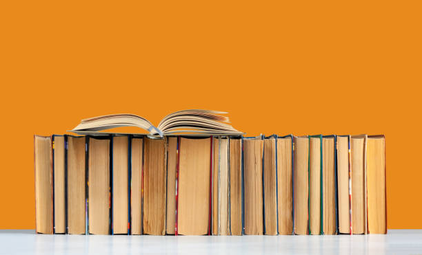 istock Open hardback book, diary, fanned pages on stack of books on white table in library. 1256532333