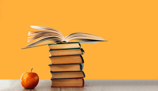 istock Open hardback book, diary, fanned pages on stack of books on white table in library. 1256532357