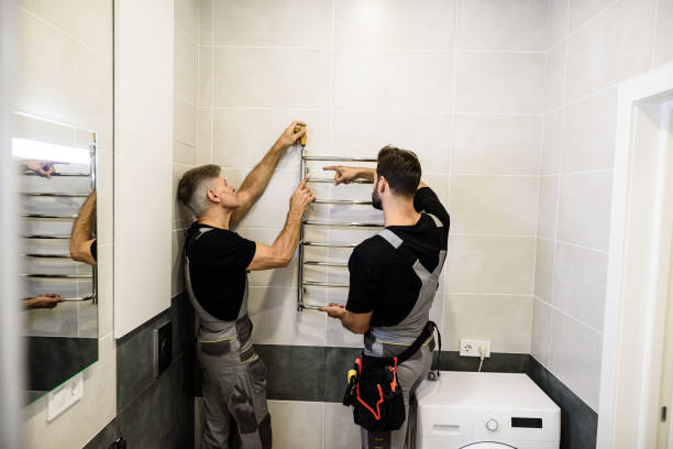 istock Two plumbers, workers in uniform working, installing towel rail, electric towel dryer on the bathroom wall using screwdriver. Construction, maintenance and repair concept 1256532435