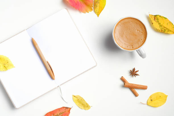 istock Autumn flat lay composition. Cup of coffee, opened paper notebook with pen, cinnamon sticks, fallen leaves on white wooden desk. Autumn, fall concept. Hygge, comfort, cozy home desk. Top view 1256533035