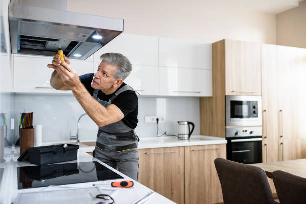 Make your life easier. Aged repairman in uniform working, fixing broken kitchen extractor fan using screwdriver. Repair service concept Aged repairman in uniform working, fixing broken kitchen extractor fan using screwdriver. Repair service concept. Selective focus.
