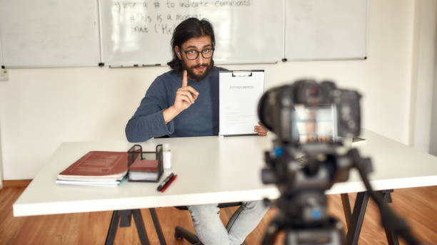 istock Young caucasian male teacher looking at camera and gesturing, teaching Python online, recording video lesson at home. Focus on a man 1256533756