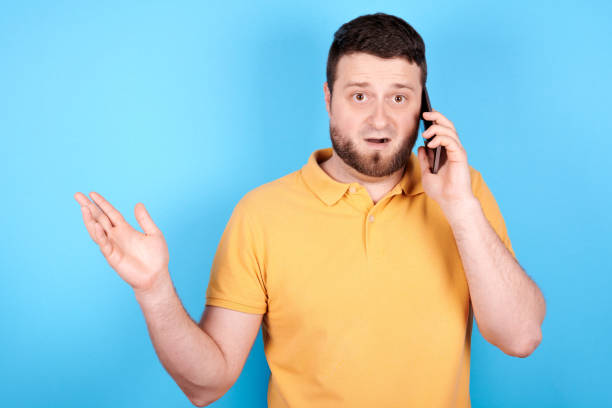 istock Angry brunette man screaming in mobile phone, rage and mad expression. Isolated on blue background. 1256533787