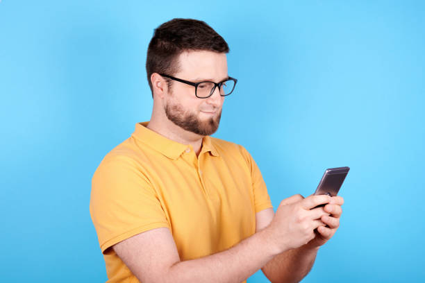 istock Brunette man with glasses using mobile phone, chatting. Isolated on blue background. 1256534555