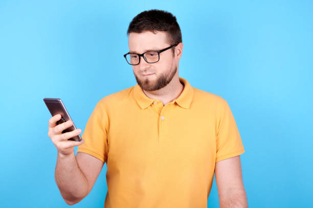 istock Brunette man with glasses using mobile phone. Isolated on blue background. 1256534579