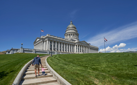 Father and daughter walking towards the Utah State Capitol Building in Salt Lake City during a warm summer day.