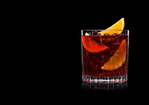 Negroni Cocktail in crystal glass with ice cubes and orange slices onblack background. Space for text