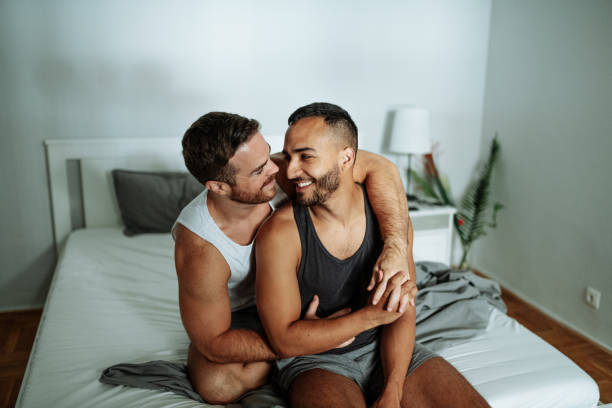 coppia gay in camera da letto durante il lockdown abbracciandosi e baciandosi al mattino - sensuality people mobile phone 30s foto e immagini stock