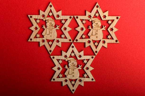 Three light brown wooden snowflakes on vivid red textured cardboard background, displayed on left and bottom, top view with space for text on right, flat lay with laser cut wooden objects tres copos de nieve de madera marrón claro sobre fondo de cartón texturizado rojo vivo, que se muestra en la izquierda y en la parte inferior, vista superior con espacio para el texto a la derecha, plano yacía con objetos de madera cortados por láser