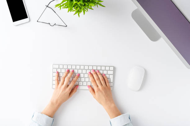 istock Office desktop concept. Woman’s hands working on computer with business accessories on white background. Top view 1256548115