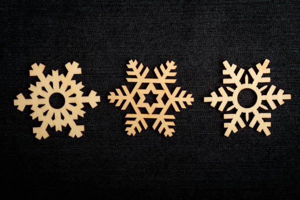 istock Three light brown wooden snowflakes on dark grey textile material background, displayed on centre, top view with space for text around, flat lay with laser cut wooden objects, selective focus 1256548125