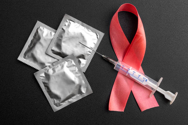 istock Red ribbon with condoms and syringe on black. Aids issues. 1256548433