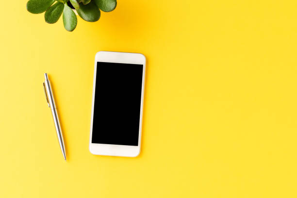 istock Business background with mobile phone with empty screen on yellow table. Office desktop with accessories 1256548650