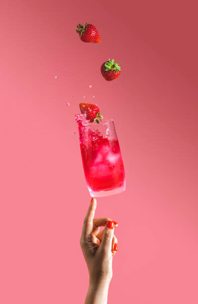 Woman hand support fly glass of strawberry drink with splash, juice strawberries falling in glass. Summer art food concept on pink background stock photo