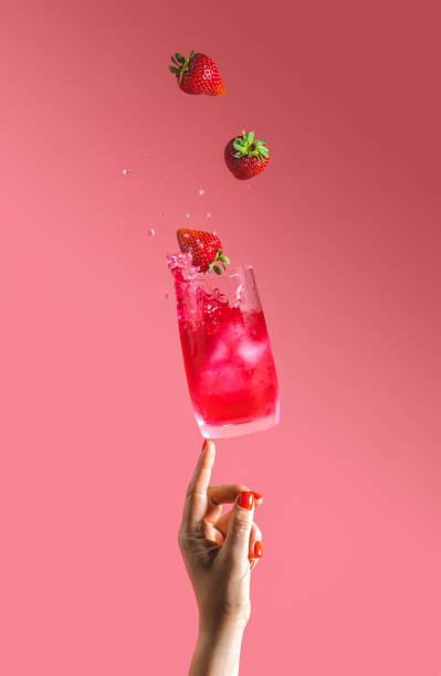 woman hand support fly glass of strawberry drink with splash, juice strawberries falling in glass. summer art food concept on pink background - drink ice splashing spray imagens e fotografias de stock