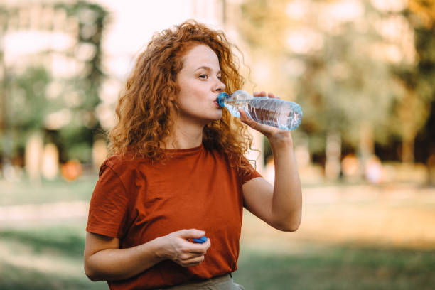 spragniona młoda ruda kobieta pijąca wodę - young adult lifestyles city life drinking zdjęcia i obrazy z banku zdjęć