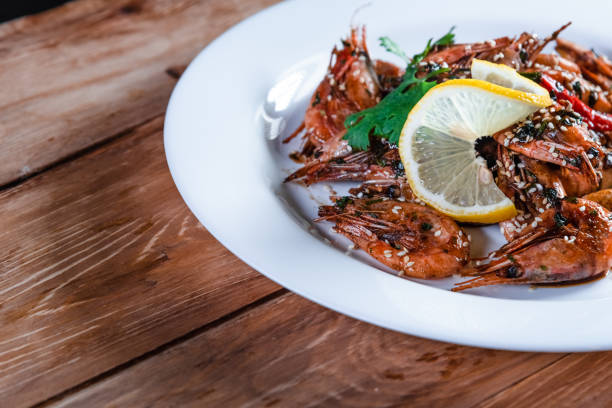 istock Appetizing fried shrimp with specialties, sesame seeds and lemon, on a white plate on a background of wood. Food concept in restaurants and bars 1256553509