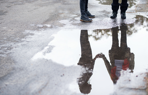 Reflection of two women standing by a water puddle on road outdoors
