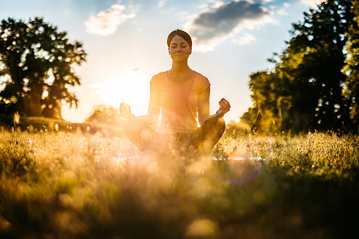Portrait of young serene woman doing meditation in nature at sunrise or sunset.
