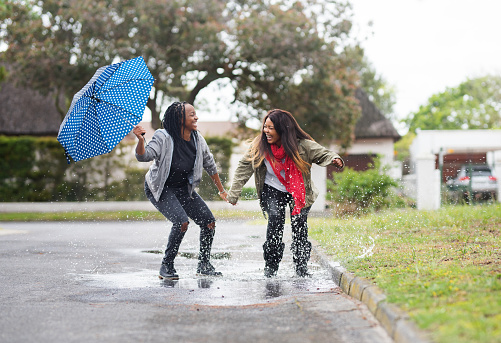 Shot of two young women jumping in the puddle of water outdoors on a rainy day
