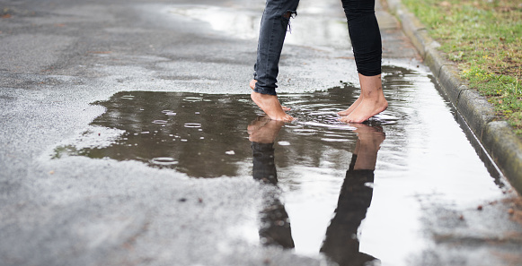 Close-up to two women standing barefoot on puddle on road