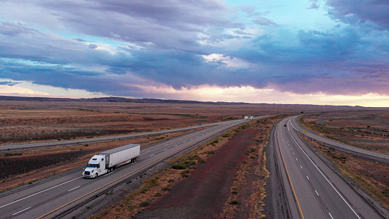 Long Haul Freight Hauler Semi-Truck and Trailer Traveling on a Four-Lane Highway in a desolate desert at dusk or dawn